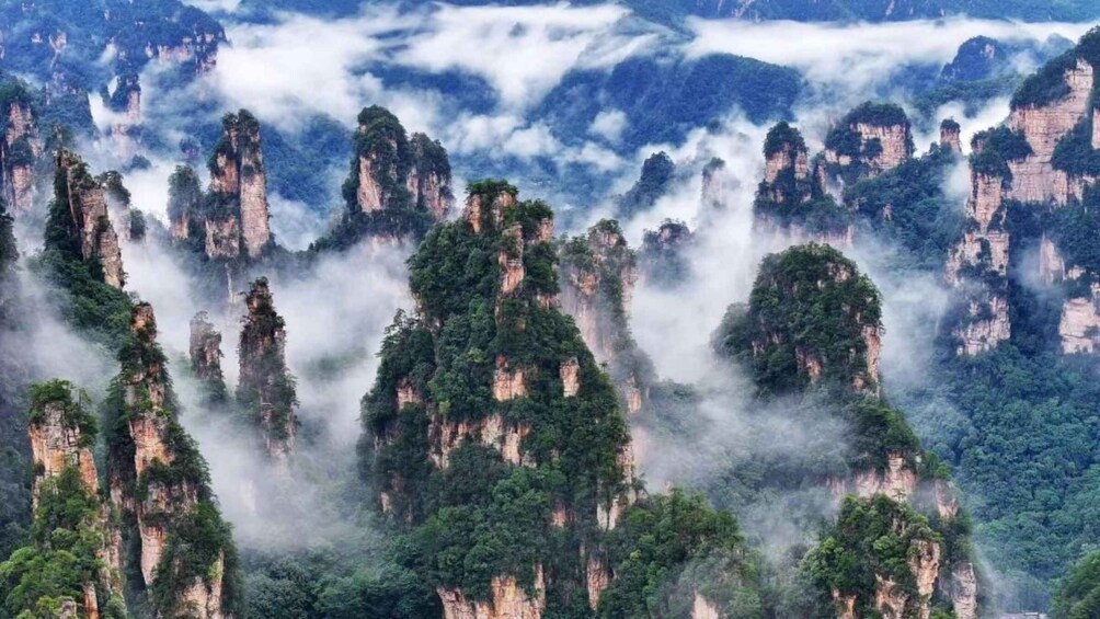 Towering limestone peaks with dense forest coverage and mist enveloping the landscape. 5