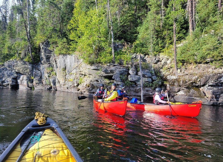 Three people kayaking on a river surrounded by rocky cliffs and dense forest. 4