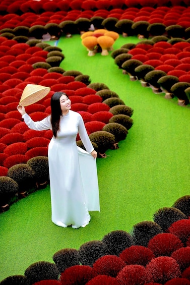 A woman in a white dress standing in a garden with red and green spherical plants. 5