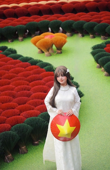 A person in a white dress holding a red and yellow object, standing in a field with rows of red and green plants. 4