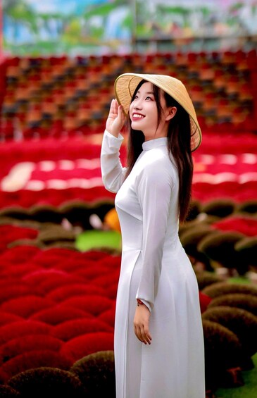 A person in a white dress and straw hat standing in a field of red flowers. 4