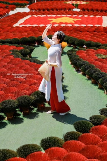 A person standing in a field of red flowers with green bushes, wearing a white top and red skirt. 1