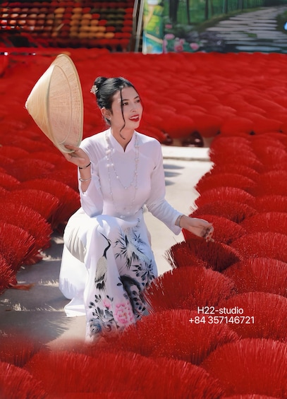 A person in traditional attire holding a conical hat, walking through a field of red flowers. 2
