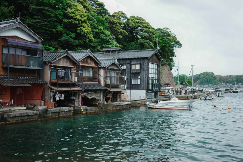 Traditional wooden houses by a calm river, a dock with a boat, and lush greenery in the background. 3
