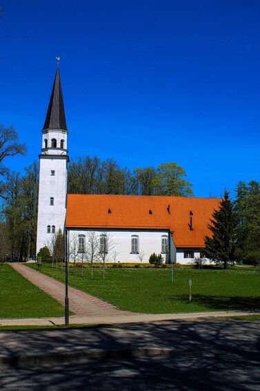 A church with a tall tower and a red roof, surrounded by a green lawn and trees. 1