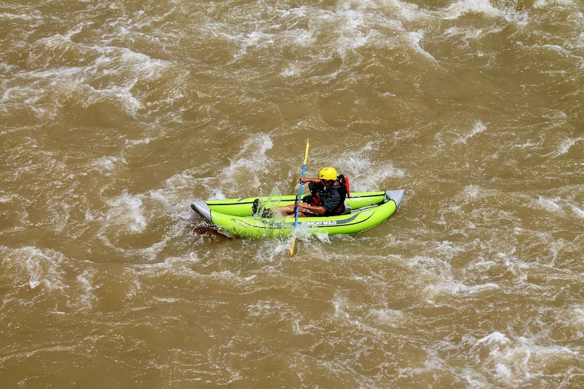 A person in a green kayak paddling through choppy brown water. 1