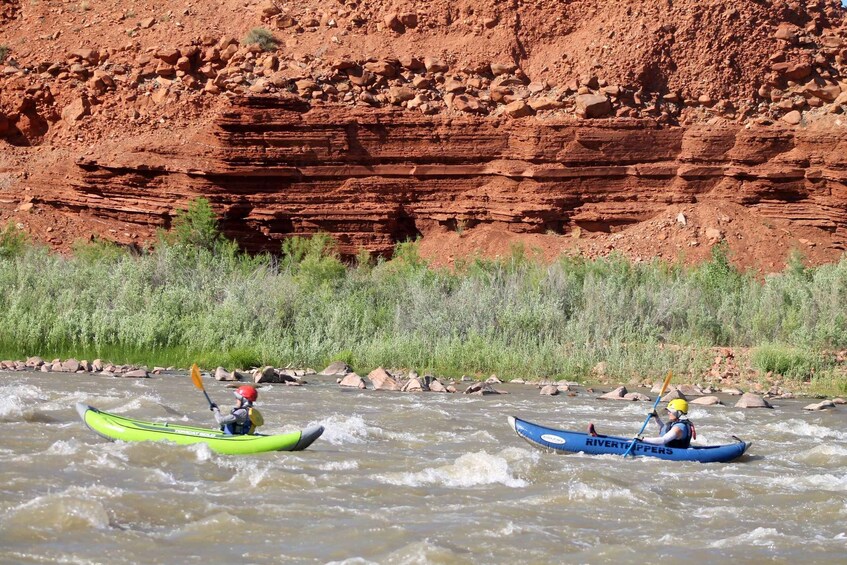 Two kayakers on a river with red rock cliffs in the background. 4