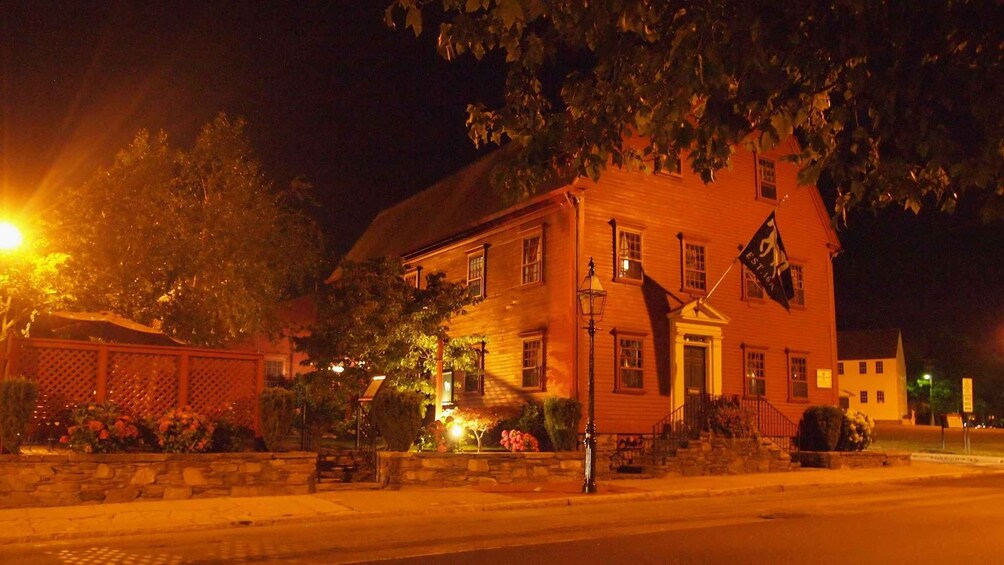 A historic building with a flag, illuminated by street lamps, surrounded by trees and a stone wall. 2