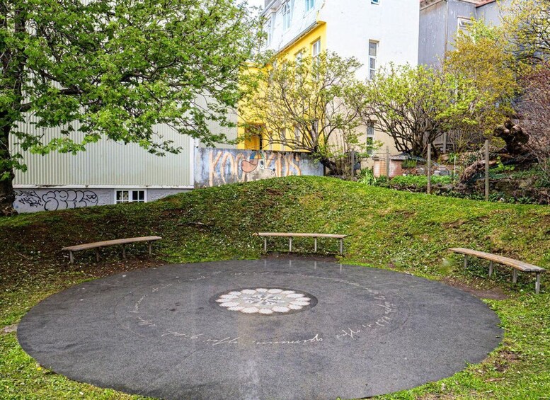 A circular paved area with benches, surrounded by greenery and buildings. 4