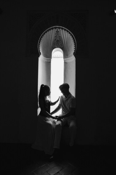 A couple sitting by a window with intricate wall patterns. 2