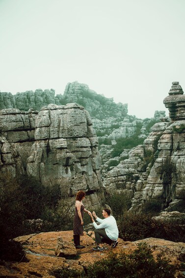 A person kneeling on a rock with another standing nearby in a rocky landscape. 4