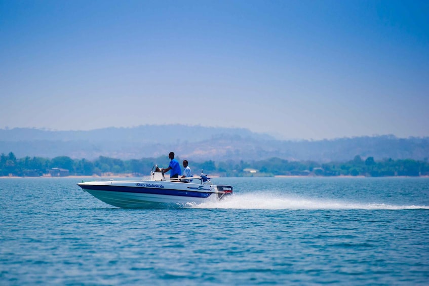 A speedboat with two people on the water, with a hilly landscape in the background. 4