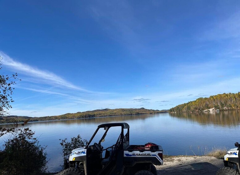 A white ATV with 'RANGER' and 'KANGSCAT' on it, parked by a calm lake with trees and hills in the background. 1