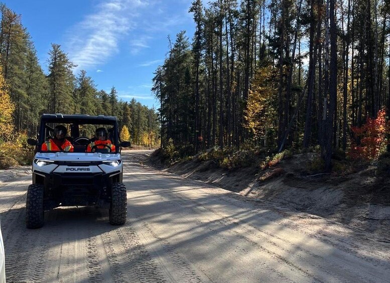 A Polaris ATV on a dirt road surrounded by a forest with autumn foliage. 5