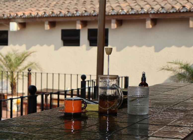 A glass pitcher, a mug, and a bottle on a metal table outdoors. 2