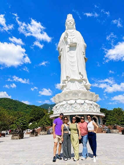 A large white statue of a figure in traditional attire, surrounded by a lotus-shaped base, with a clear blue sky and green hills in the background. 5