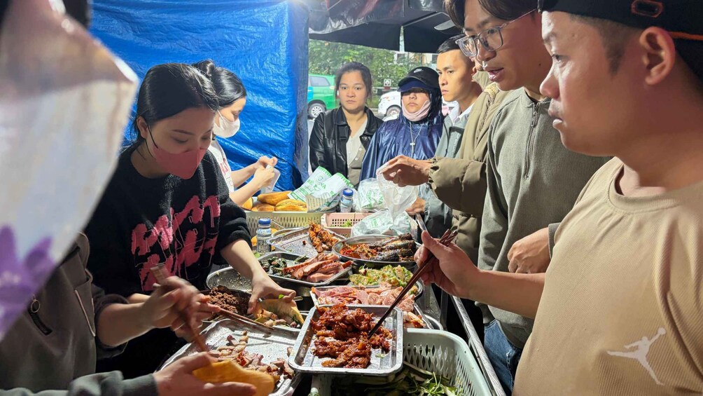 A group of people serving themselves food at a street food stall. 1