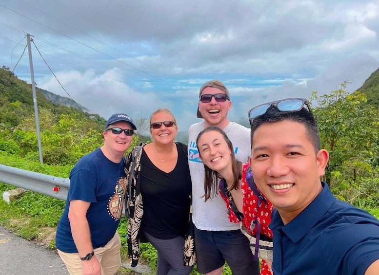 A group of people taking a selfie on a road with a mountainous landscape in the background. 1