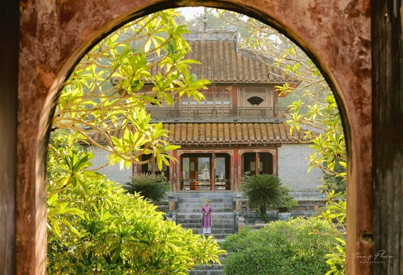 A traditional building with a tiled roof, a statue in front, and lush greenery. 2