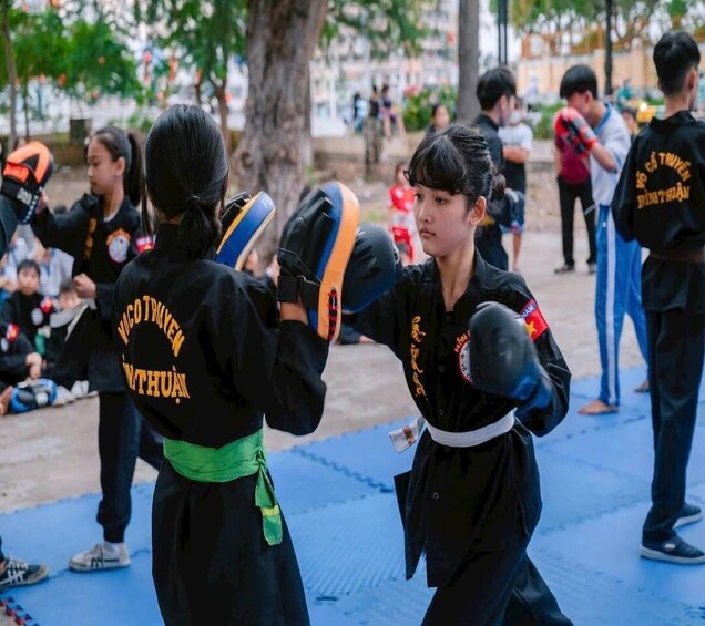 Two individuals practicing martial arts on a blue mat outdoors. 1