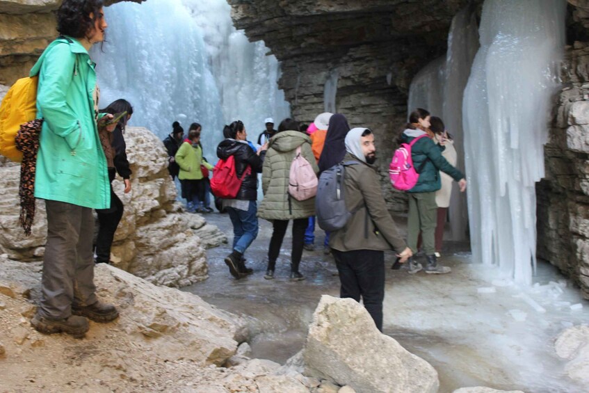 A group of people walking near a large ice formation in a rocky area. 3
