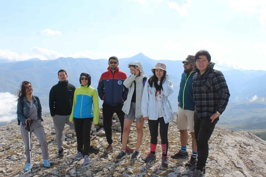 A group of people standing on a rocky mountain peak with a mountain range in the background. 1