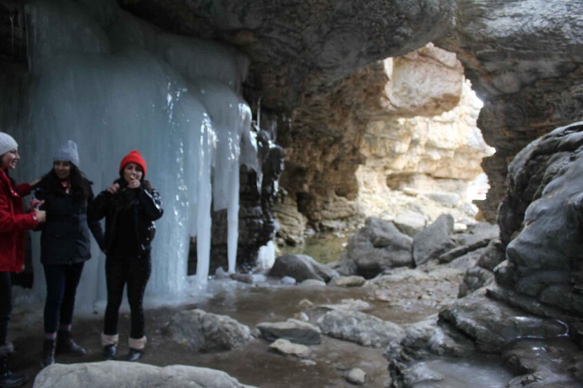 A group of people standing near a frozen waterfall in a rocky cave. 4