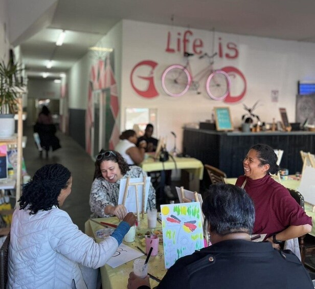 A group of people engaged in an art activity in a room with a wall sign that reads 'Life is Good.' 2