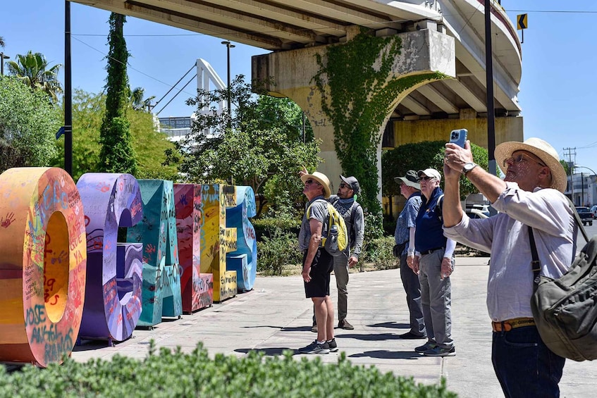 A group of people taking photos, colorful cylindrical structures with graffiti, and a bridge in the background. 1