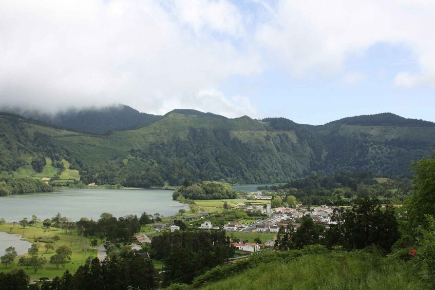 A lake surrounded by lush green hills, a small town in the foreground, and a cloudy sky. 2