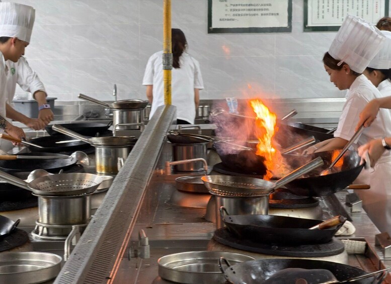A professional kitchen with chefs cooking over a large wok on an open flame. 2
