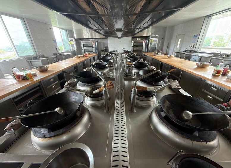 A commercial kitchen with multiple gas stoves, stainless steel sinks, and a central ventilation system. 3
