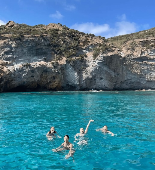 A group of people swimming in clear turquoise water with rocky cliffs in the background. 3