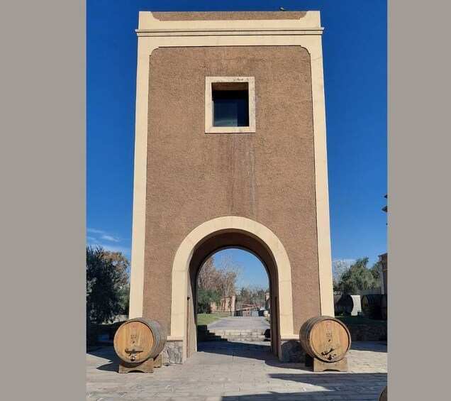A tall, beige brick structure with an arched entrance and two wooden barrels at its base. 4
