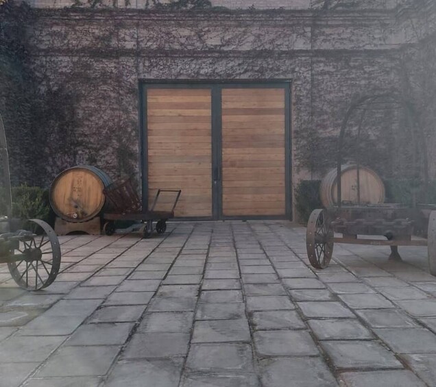 A courtyard with a wooden door, stone paving, and two wooden barrels. 5