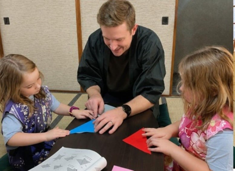 Three people sitting at a table with papers and colored paper. 3