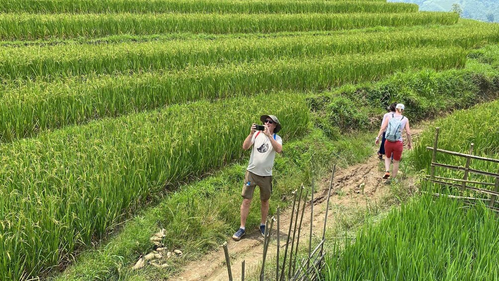 A person taking a photo in a rice field with another person walking beside them. 5