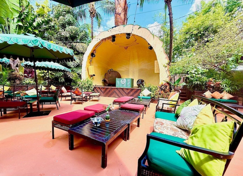 An outdoor seating area with tables and chairs, surrounded by lush greenery and a large arched structure. 4