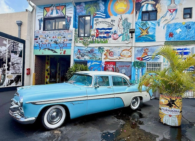 A vintage blue car parked in front of a building with colorful murals. 3