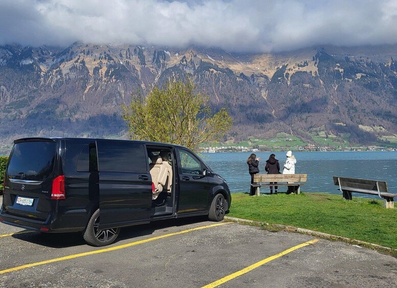 A black van parked by a lake with mountains in the background. 2