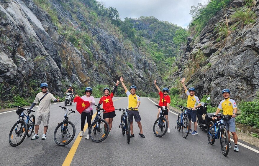 A group of cyclists on a road with rocky cliffs and greenery on both sides. 3