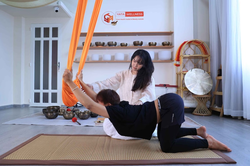 A person performing an aerial yoga pose with an instructor. 5