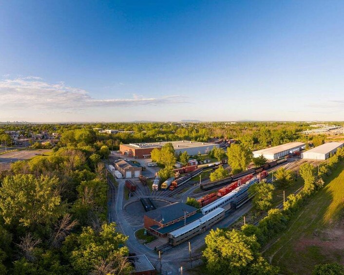 An aerial view of a train yard with multiple tracks and trains, surrounded by trees and industrial buildings. 1