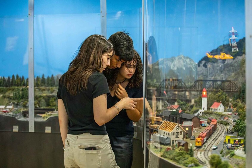 Two people observing a model train exhibit with a mountainous landscape and a bridge in the background. 5
