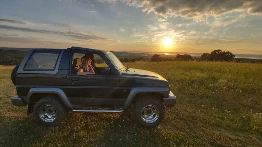 A black SUV parked on a grassy field with a sunset in the background. 1