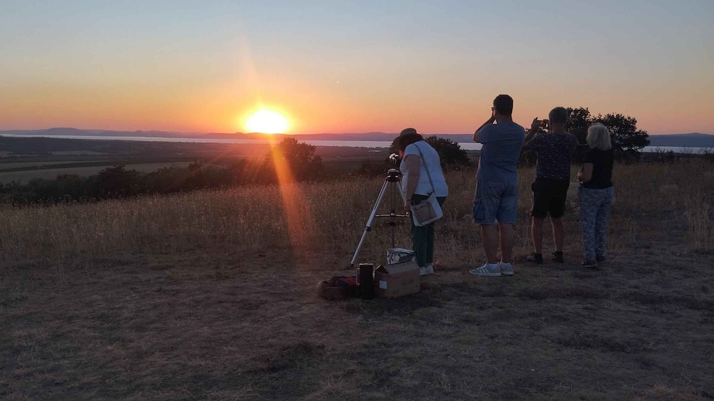 A sunset over a grassy field with a group of people observing the sun. 2