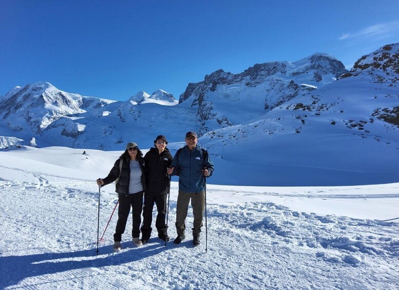 Three people standing on a snow-covered mountain with a clear blue sky. 3