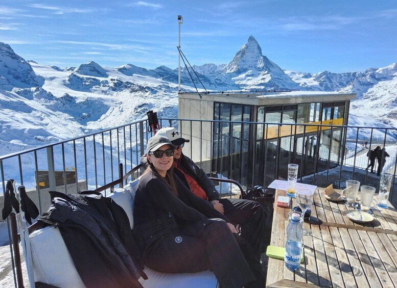 A person seated on a chair with a mountain view, a table with a bottle, and a glass. 5