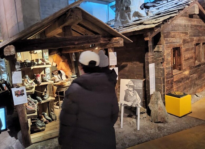 A person in a black jacket and white cap standing in front of a wooden house display with a shoe rack and a chair. 4