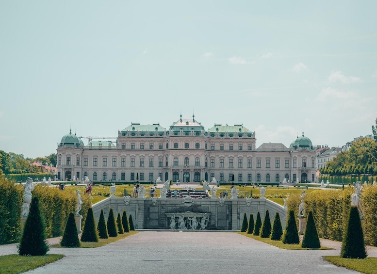 A large classical building with a central dome and symmetrical wings, surrounded by manicured gardens and statues. 1